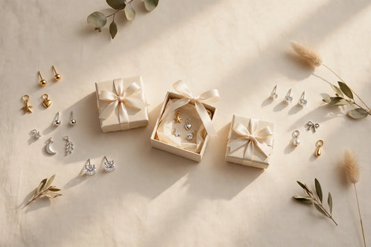 Early-afternoon flat-lay of small stud earrings, crystal studs and jewelry charms with cream gift boxes and ribbons on a warm cream background